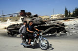 ACH100486M
Syrian men drive a motorbike past a destroyed T-72 battle tank.