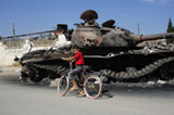 ACH100487M
A Syrian boy on his bicycle in front of a destroyed T-72 battle tank.