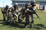 STK105779M
Soldiers dressed in chemical warfare gear carry equipment.