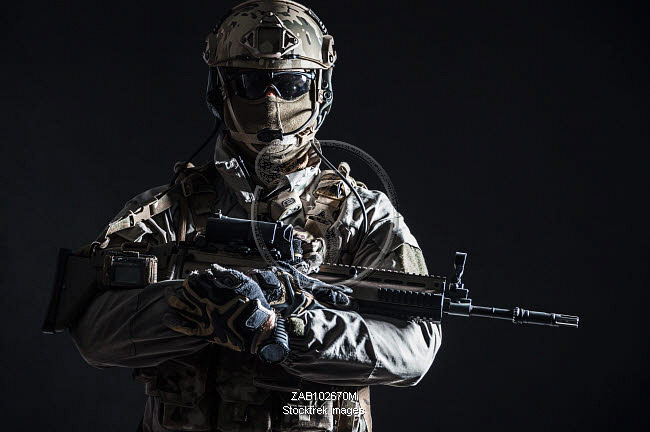 Dark contrast studio shot of Army soldier holding assault rifle ...